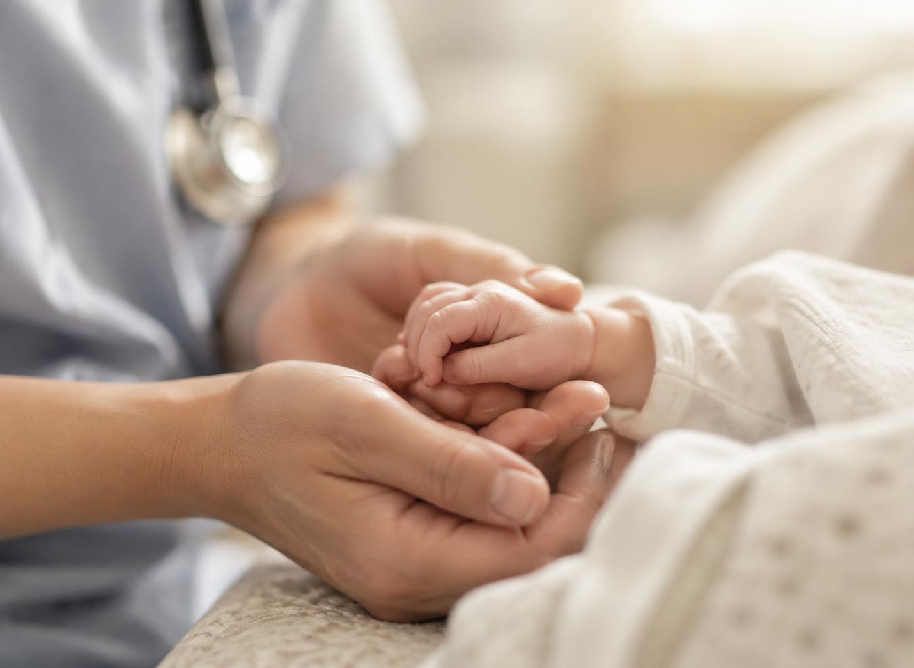 A caregiver gently holding a newborn baby's hand — representative image